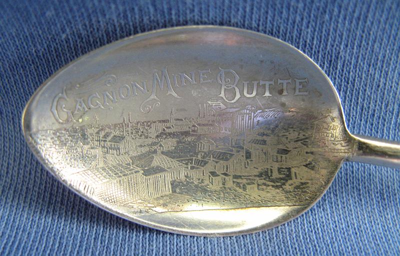 Souvenir Mining Spoon Bowl Gagnon Mine Butte MT.JPG - SOUVENIR MINING SPOON GAGNON MINE BUTTE MT - Sterling demitasse spoon with engraved bowl showing mining scene and marked GAGNON MINE BUTTE, unusual wire wrap handle, 4 in. long, reverse marked Sterling with scroll S hallmark for Simons Brothers Philadelphia, PA who made Sterling spoons from 1840 to 1908  [The Gagnon Mine, located on the western side of Butte, MT in Silver Bow County, is one of the oldest and most productive of the Butte copper mines.  Like many of the Butte properties in the very early years of mining development, the Gagnon Mine ownership was contentious.  The small settlement of Gagnon was formed by Patrick Meagher and Antoine Gagnon just outside the town site limits of Butte on Feb. 21, 1877. They filed a claim on the property but the land was apparently owned by J. C. C. Thornton who purchased it in 1869.  The courts sided with Thornton but he failed to represent the claim within the one-year period to maintain ownership.  Meagher and Gagnon relocated the claim and named it the Gagnon claim.  Thornton along with John Rosenfeld, Joel W. Ransom and Timothy Kelly bought the claim from Meagher and Gagnon and proceeded to develop a mine.  These early claims along the copper rich Parrot lode that included the Park, Parrot, Original and Gagnon were filed as early as 1864. However it was the construction of local smelting operations in 1879 that triggered the expansive Butte copper production.  Copper King William A. Clark formed the Colorado and Montana Smelting Co. in May 1879 and purchased the Gagnon Mine.  Reorganized in 1883 as the Colorado Smelting and Mining Co., the company mines included the Gagnon, Original, Caledonia, Nettie, Hibernia and Burlington.  The Gagnon was the main producer and was particularly rich in silver and gold along with copper. The name of the company was once again changed circa 1905 to the Trenton Mining and Development Co. as organized under laws of New Jersey with a capitalization of $2,500,000. The Trenton was controlled through ownership of the entire stock issue by Amalgamated Copper Co. The company employed John D Ryan as managing director, John Gillie as general superintendent, and Geo F McGee as mine superintendent. At the time, Trenton owned 35 quartz and placer claims and an area of 220 acres in the western limits of the Butte copper zone including the Gagnon Mine carrying argentiferous and highly zinciferous copper ores averaging 2.75 copper and 3.5 oz silver per ton.  The Gagnon Mine had a 2,300 foot three compartment shaft sunk at an angle of 74 degrees and was connected underground with the Original Mine.  In 1910 the Trenton Company was purchased by the expanding Anaconda Copper Mining Company.]